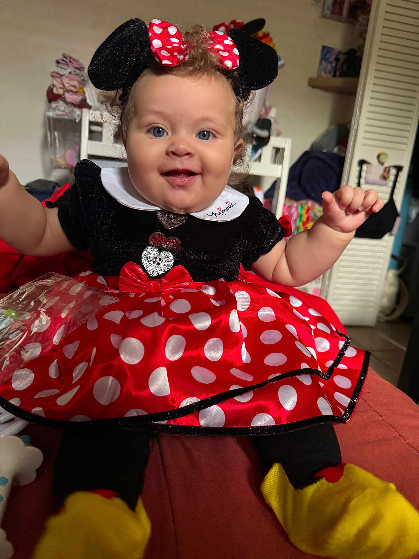 Rayne is registered to the contest to win money with this photo: baby, child, costume, minnie_mouse, dress, polka_dots, headband, smile, blue_eyes, curly_hair, indoors, chair, clothing, person, cute, happy, sitting, toy, footwear, playful