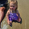 child, girl, toddler, portrait, purple_outfit, dress, sitting, outdoors, sunlight, wet_surface, water, swimming_pool, summer, blonde_hair, ponytail, smiling, adult, family, reflection, photography