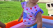Emryn is registered to the contest to win money with this photo: child, toddler, girl, smiling, portrait, outdoor, backyard, swimming_pool, inflatable_pool, water, swimsuit, strawberry_pattern, summer, sunny, grass, brick_wall, playtime, splashing, family, happy