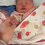Hope is registered to the contest to win money with this photo: newborn, baby, sleeping, infant, portrait, face, blanket, swaddled, hand, parent, fingers, hospital, wristband, strawberry, floral_pattern, pink, blue, indoors, close_up, cozy