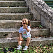 Ella a rejoint le concours — aidez-le/la à gagner de superbes lots ! child, toddler, laughing, leaf, outdoor, stone_steps, grass, greenery, casual_clothing, white_shoes, pigtails, nature, sunlight, happy, playful, sitting, daylight, old_stone, smile, person