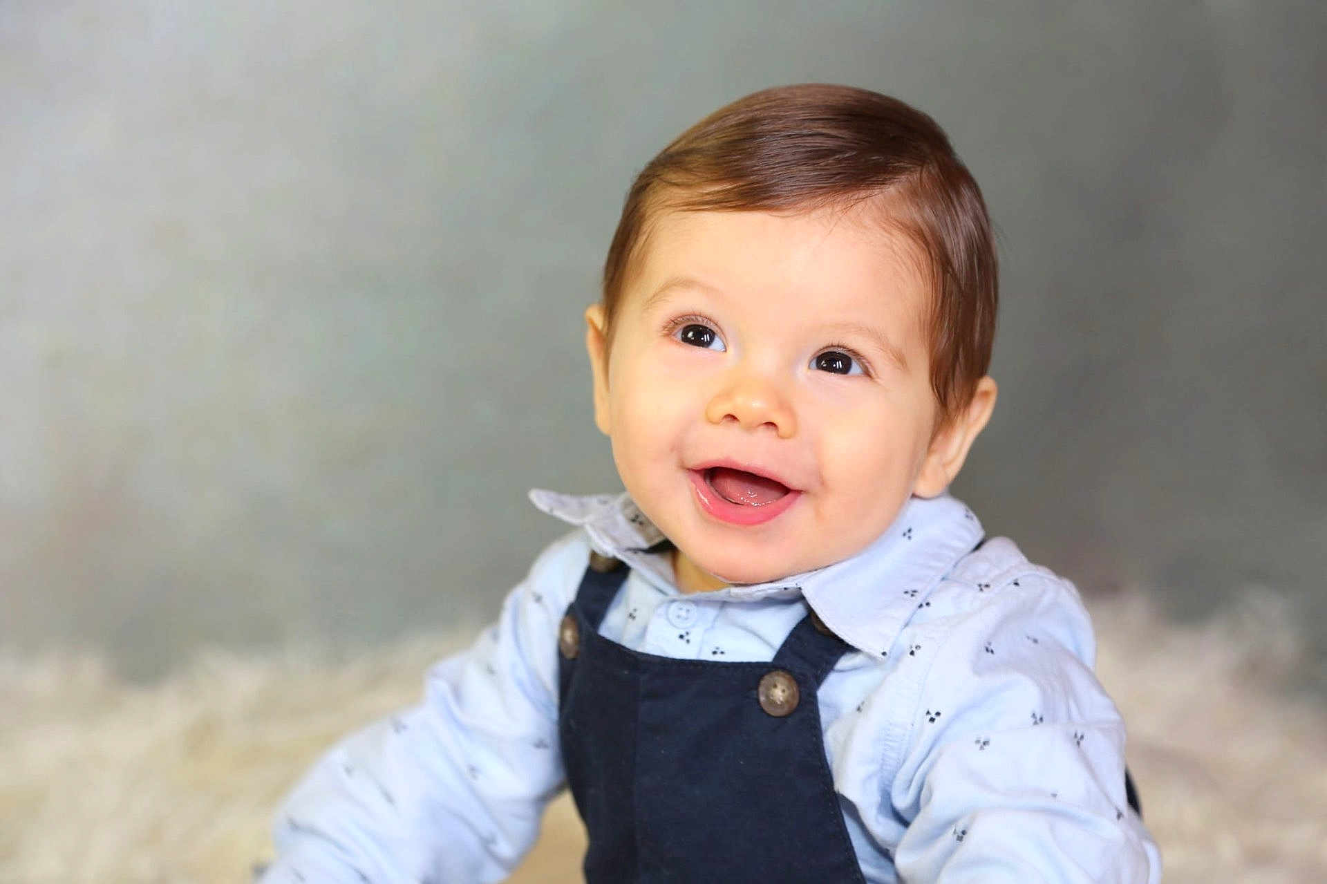 Leeroy a rejoint le concours — aidez-le/la à gagner de superbes lots ! baby, child, smiling, portrait, face, blue_shirt, overalls, happy, indoor, studio, infant, cute, young_child, short_hair, buttoned_shirt, light_background, fur_rug, person, closeup, expression
