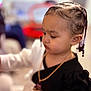 beads, black_clothing, blurred_background, braided_hair, casual, child, cute, earrings, face, hand, indoor, necklace, person, portrait, side_view, skin, soft_lighting, toddler, young_child, youth