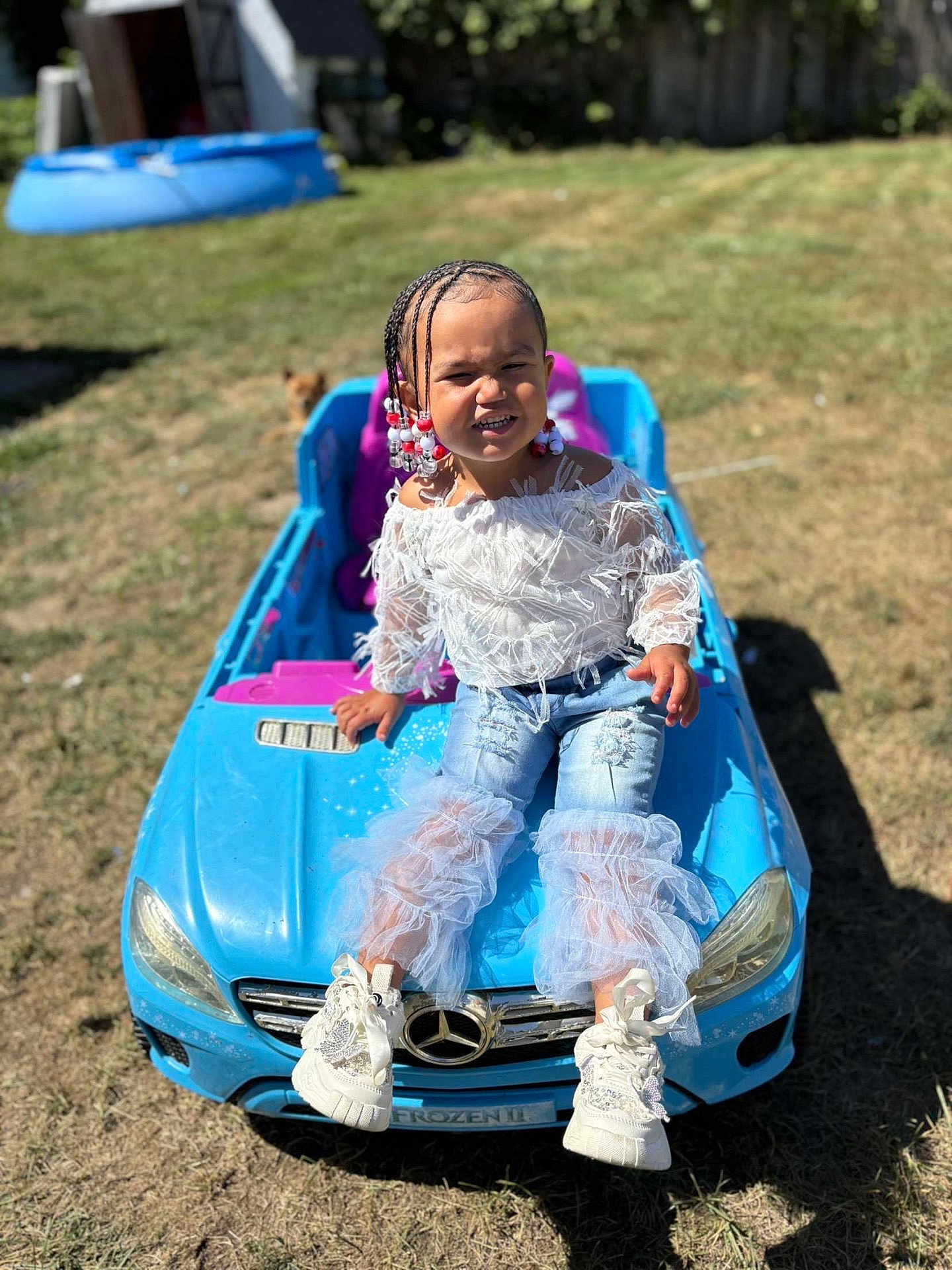 Kaioni is registered to the contest to win money with this photo: beads, blue, braids, child, fashion, fence, grass, grimace, kiddie_pool, outdoor, person, playful, ripped_jeans, ruffles, sneakers, summer, sunny, toy_car, white_top, yard
