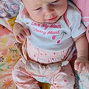 Luna is registered to the contest to win money with this photo: baby, infant, child, pink_clothing, patterned_pants, white_shirt, cherry_design, blanket, colorful, cute, indoors, sitting, footwear_free, curious_expression, soft_light, small_hands, head, face, young_child, cozy