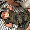 baby, infant, pacifier, camo_clothing, mittens, black_hat, blanket, patterned_blanket, lying_down, arm, adult, resting, cute, infant_clothing, child, person, indoor, soft_fabric, comfort, close_up