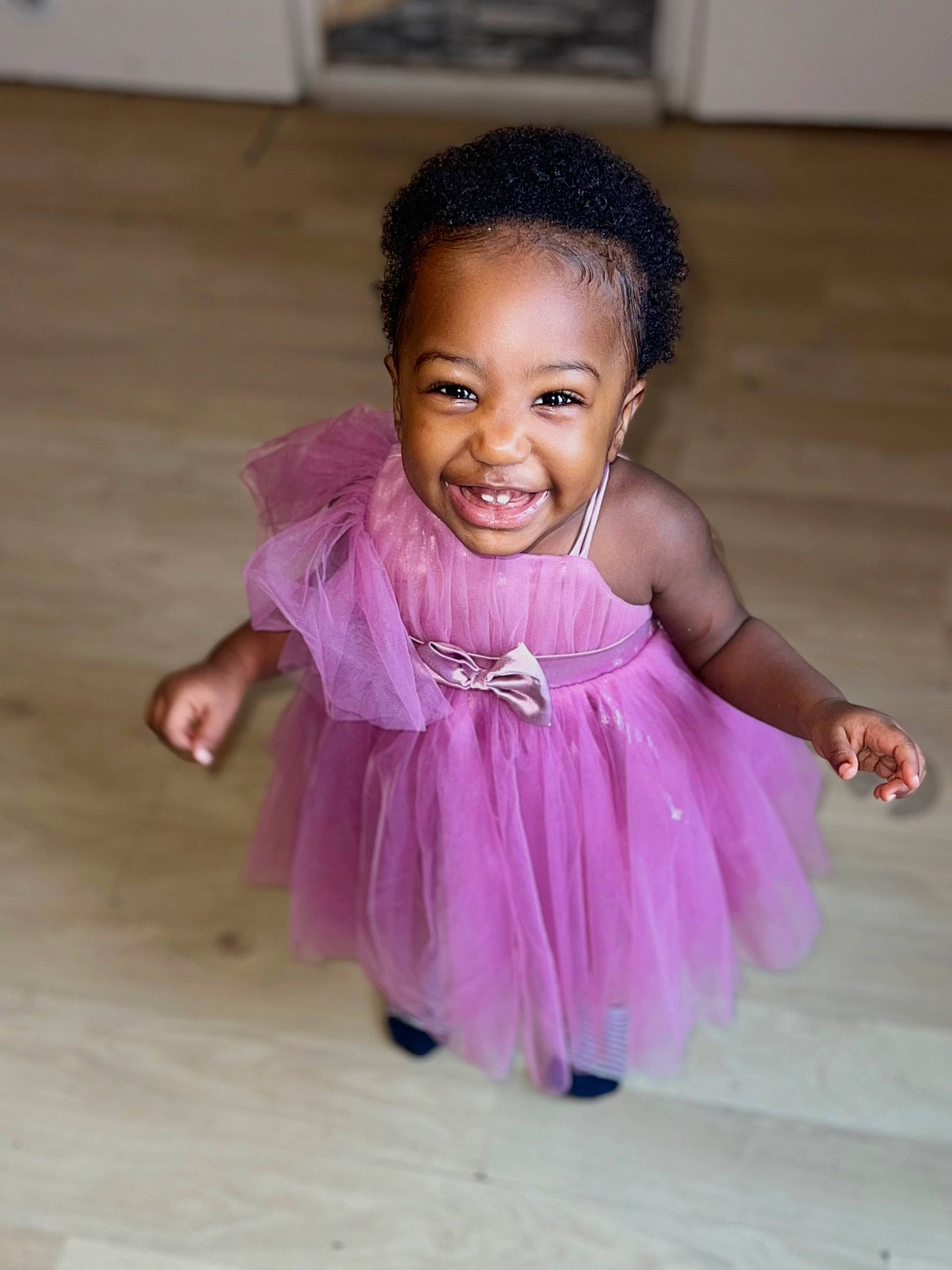 Ariana participe au concours pour gagner de l'argent avec cette photo : baby, baby_toddler_clothing, cheek, child, dress, event, flooring, fun, happy, hardwood, head, joy, magenta, person, pink, purple, sitting, skin, smile, sock