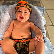 Antonio is registered to the contest to win money with this photo: baby, infant, smiling, crocheted_hat, crocheted_diaper_cover, blanket, drool, happy, playful, skin, legs, hand, face, indoor, tile_floor, cute, child, expression, lying_down, apparel