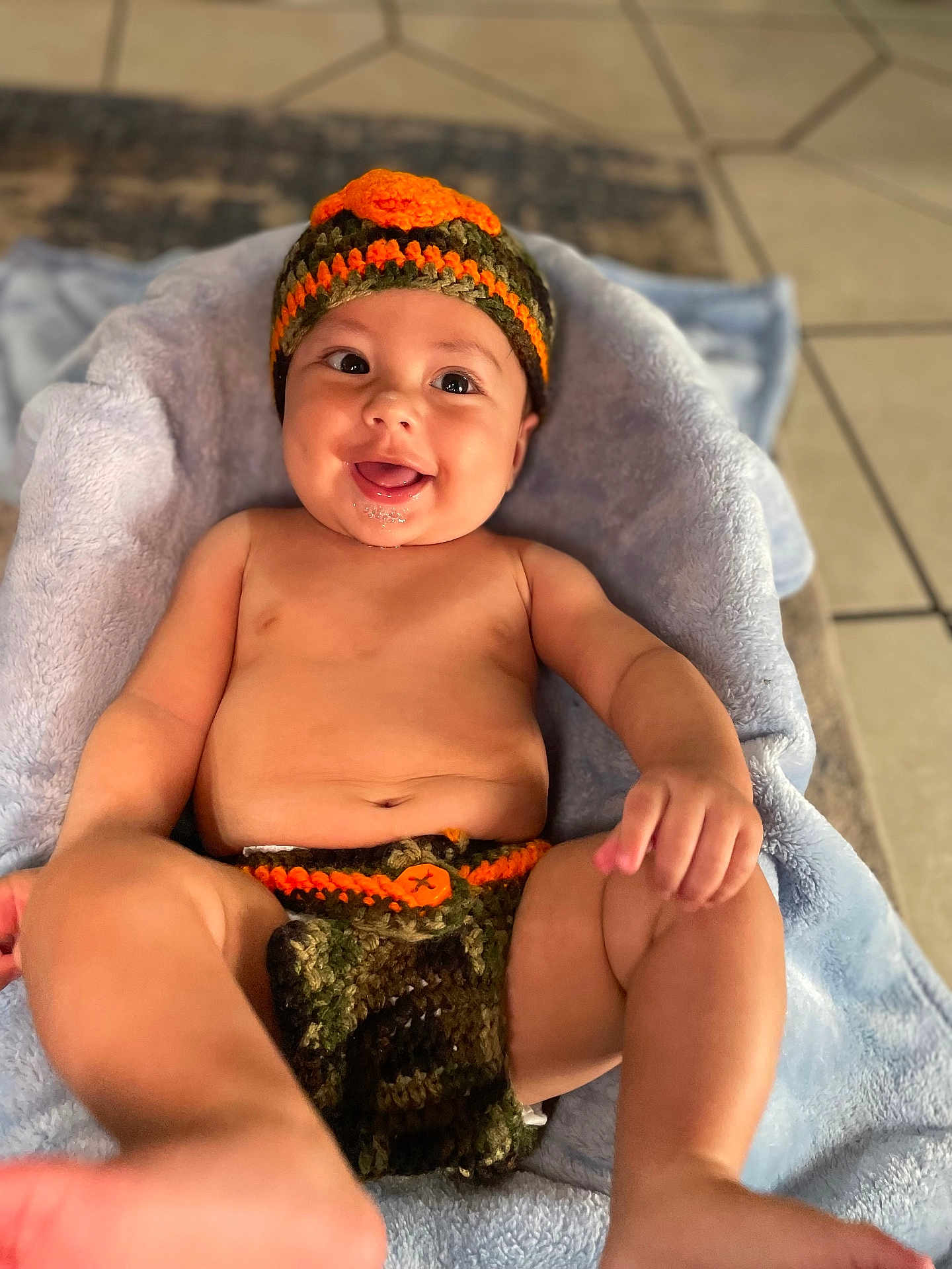 Antonio is registered to the contest to win money with this photo: baby, infant, smiling, crocheted_hat, crocheted_diaper_cover, blanket, drool, happy, playful, skin, legs, hand, face, indoor, tile_floor, cute, child, expression, lying_down, apparel