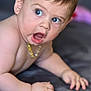 baby, child, blue_eyes, curly_hair, bead_necklace, skin, expression, mouth_open, hand, mat, floor, indoors, portrait, cute, infant, candid, lying_down, closeup, person, young