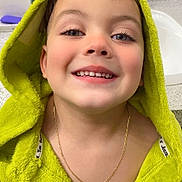 Yeison is registered to the contest to win money with this photo: child, smiling, face, hooded_towel, green_towel, gold_chain, tablet, bathroom, sink, counter, bottle, toothbrush, hygiene, young_child, portrait, happy, indoor, casual, closeup, person
