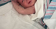 Marvin is registered to the contest to win money with this photo: newborn, baby, hospital, crib, blanket, infant, bed, medical_equipment, person, wrapped, linen, sleeping_area, small_arm, head, face, resting, cute, indoors, healthcare, patient