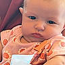 baby, infant, child, portrait, face, eyes, blond_hair, pink_clothing, floral_pattern, strawberry_pattern, bib, baby_seat, close_up, indoor, sitting, looking_at_camera, soft_lighting, cute, head, photograph