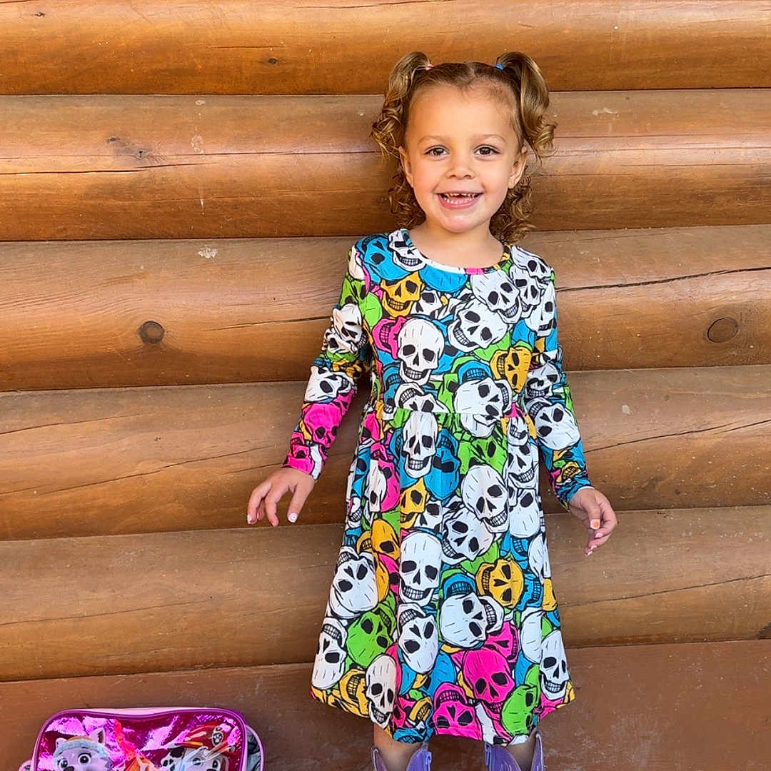 Brinlann is registered to the contest to win money with this photo: child, colorful, cowboy_boots, curly_hair, cute, dress, floor, girl, happy, log_cabin, outdoor, paw_patrol, pigtails, pink_bag, portrait, purple_boots, skull_pattern, smiling, standing, wooden_wall