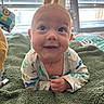 baby, smiling, infant, blanket, green_blanket, dinosaur_onesie, toy, window_blinds, indoor, happy, cute, face, child, toddler, lying_down, soft_texture, playful, bright, close_up, portrait