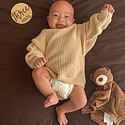Rownin joined the competition — help win amazing prizes! baby, infant, smile, sweater, diaper, teddy_bear, blanket, wooden_sign, brown_background, cute, happy, lying_down, raising_arm, milestone, child, face, person, cozy, soft_toy, newborn