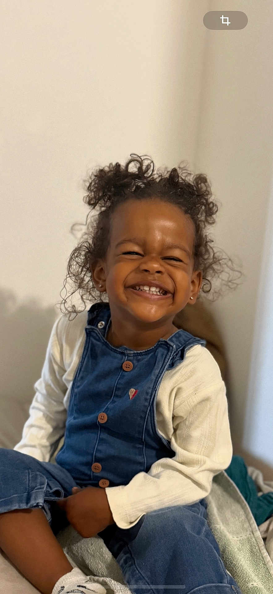 Aïcha participe au concours pour gagner de l'argent avec cette photo : child, smiling, curly_hair, denim_overalls, white_sweater, sitting, happy, indoor, portrait, cute, toddler, clothing, person, face, hair, childhood, joy, expression, casual, cozy