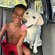 Ashton is registered to the contest to win money with this photo: boy, child, dog, white_dog, smiling, happy, tongue_out, car_interior, backseat, window, trees, sunlight, shirtless, red_shorts, pet, friendship, indoors, seat, portrait, cuddling