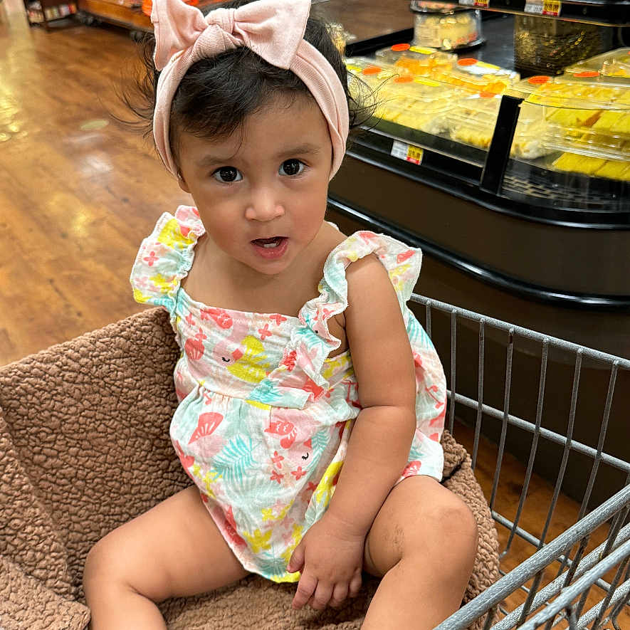 Scarlett is registered to the contest to win money with this photo: baby, bodypart, bonnet, cap, clothing, face, finger, food, grocerystore, hand, hat, head, indoors, market, person, photography, portrait, shop, shoppingcart, sweets