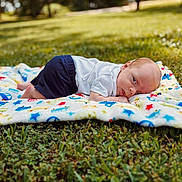 Waylon joined the competition — help win amazing prizes! baby, blanket, grass, outdoor, infant, child, nature, lawn, cute, toddler, clothing, shorts, shirt, face, head, lying_down, colorful, sunlight, peaceful, portrait