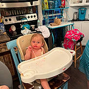 Raelynn is registered to the contest to win money with this photo: baby, high_chair, kitchen, food, messy, face, child, person, appliance, microwave, stove, teal, wooden_chair, cabinet, blanket, table, cupboard, floor, window, bottle