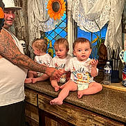 Randall joined the competition — help win amazing prizes! man, tattoo, tank_top, child, toddler, kitchen, countertop, diaper, shirt, holding_hands, window, curtains, utensils, flower, water_bottle, knife_block, wooden_spoons, sunflower, family, indoor