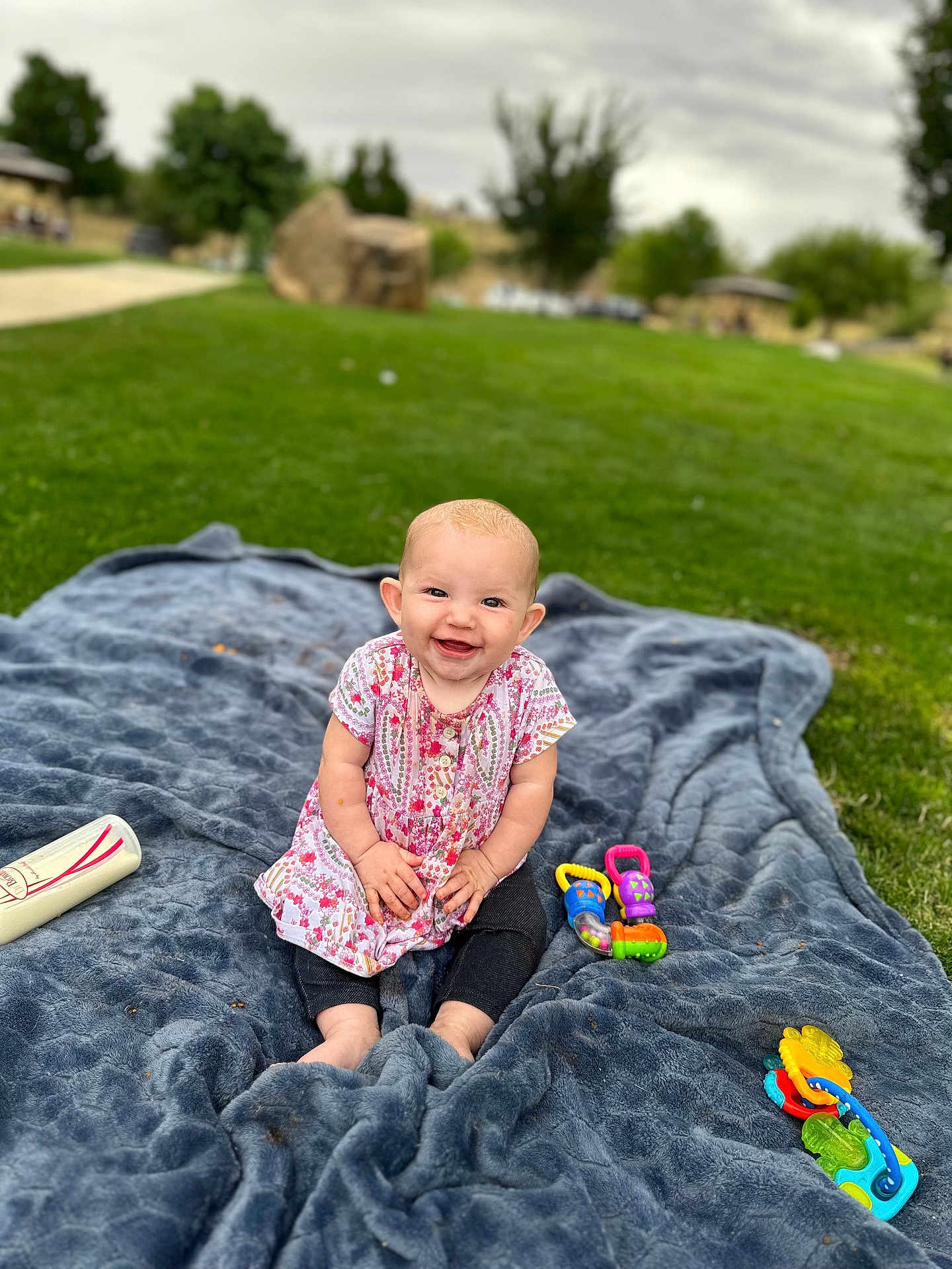 Delilah is registered to the contest to win money with this photo: baby, blanket, grass, outdoor, toy, bottle, smiling, child, park, greenery, happy, infant, toddler, clothing, nature, playtime, sitting, colorful, cute, daylight