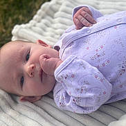 Delilah is registered to the contest to win money with this photo: baby, infant, face, hand, blanket, purple_clothing, onesie, outdoors, grass, skin, head, sleepwear, cute, newborn, portrait, lying_down, soft_texture, peaceful, young_child, natural_light