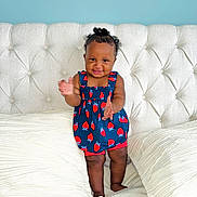Janelle joined the competition — help win amazing prizes! baby, infant, child, smile, clapping, dress, strawberry_print, navy_blue, bed, pillows, tufted_headboard, curly_hair, hair_bun, chubby_cheeks, portrait, indoor, cushion, white_bedding, happy, standing