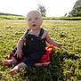 Beckham is registered to the contest to win money with this photo: baby, child, grass, outdoor, sunlight, overalls, barefoot, field, greenery, red_cloth, nature, sitting, summer, daylight, person, young, cute, holding, portrait, garden