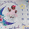 Tylynn is registered to the contest to win money with this photo: baby, infant, child, blanket, milestone, moon, flowers, pink_dress, headband, bow, numbers, star, lying_down, cute, smiling, colorful, decorative, young_child, portrait, indoors