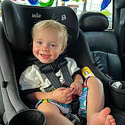 Asher is registered to the contest to win money with this photo: toddler, child, car_seat, smiling, blonde_hair, colorful_clothing, safety_harness, vehicle_interior, window, painted_letters, seat, foot, hand, cup_holder, bright, daylight, happy, casual, portrait, cute