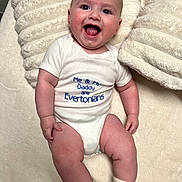 Sonny joined the competition — help win amazing prizes! baby, infant, smiling, onesie, text_on_clothing, tongue_out, cushion, blanket, soft_texture, happy, cute, child, socks, indoor, portrait, face, head, skin, limbs, comfortable