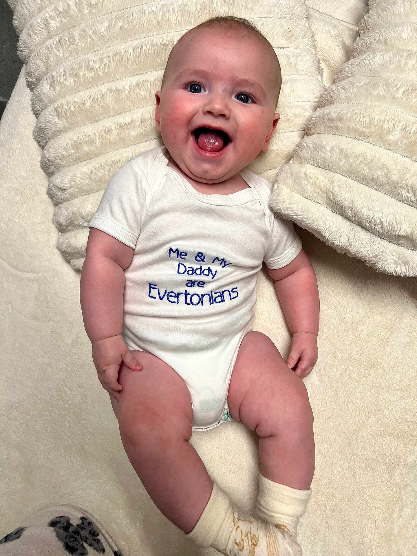 Sonny joined the competition — help win amazing prizes! baby, infant, smiling, onesie, text_on_clothing, tongue_out, cushion, blanket, soft_texture, happy, cute, child, socks, indoor, portrait, face, head, skin, limbs, comfortable