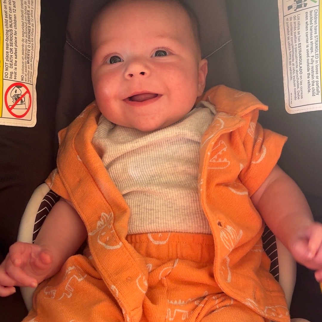 Bladon is registered to the contest to win money with this photo: baby, car_seat, casual_clothing, chicco, child, comfort, cute, expression, happy, head_and_shoulders, human, indoors, infant, one_person, orange_clothing, portrait, seat, sitting, smiling, young_child