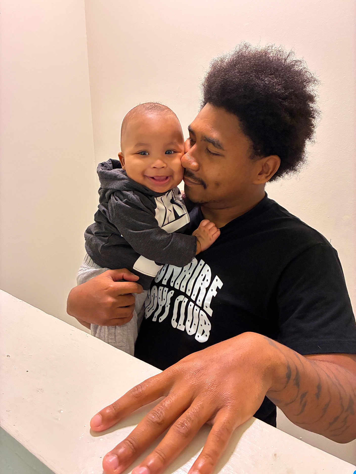 Katrell Jr is registered to the contest to win money with this photo: baby, child, man, father, smile, hug, affection, indoor, black_hair, hoodie, tattoo, hand, portrait, people, happy, love, casual_clothing, person, baby_clothes, skin