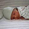 baby, newborn, infant, hat, knitted_hat, lying_down, blanket, soft_texture, green_clothing, checkered_pattern, cute, peaceful, indoors, portrait, face, small_hands, cozy, resting, young_child, sleepy_eyes