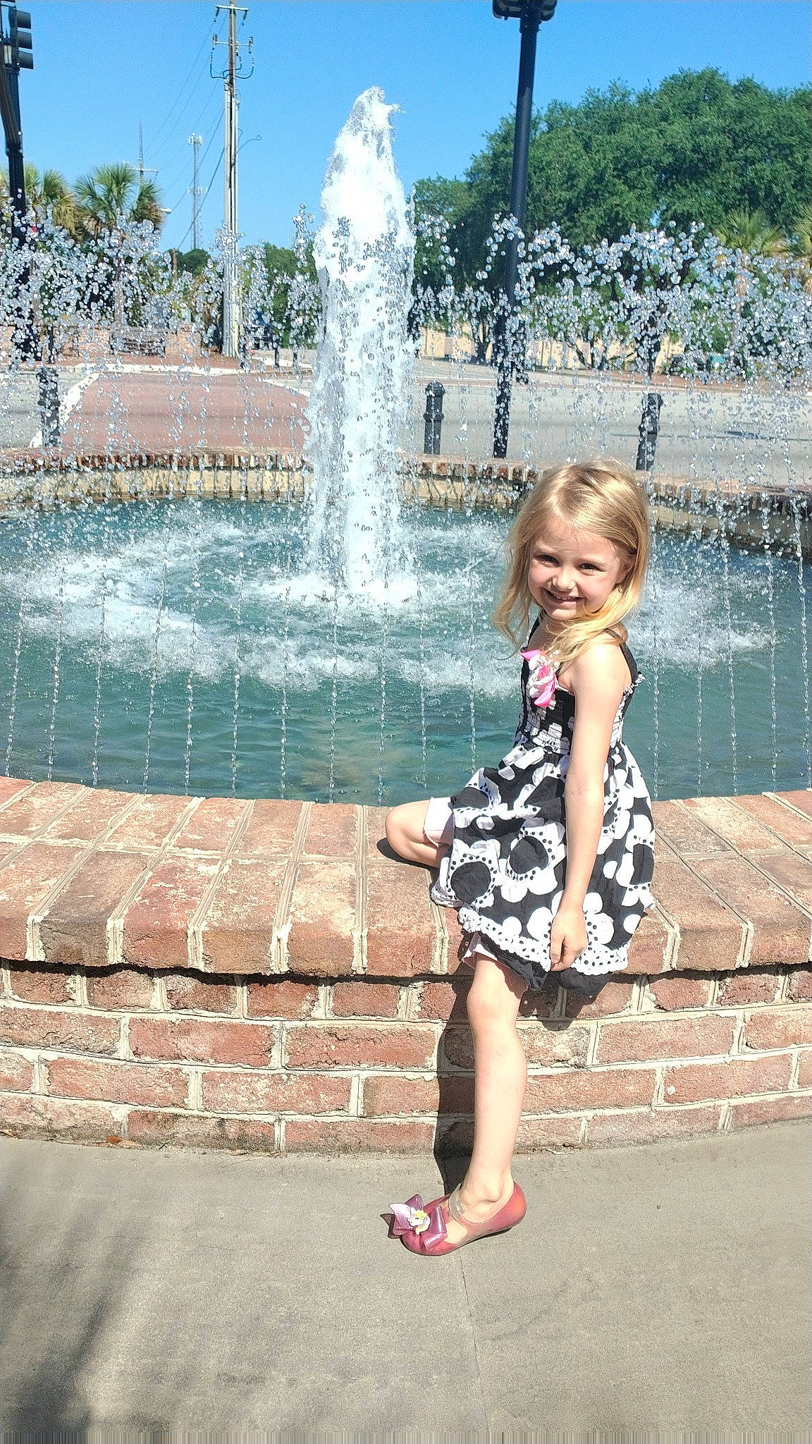 Maggie is registered to the contest to win money with this photo: beauty, daytime, dress, fountain, fun, happy, joy, leisure, line, person, photograph, public_space, recreation, sky, snapshot, standing, summer, toddler, tree, water