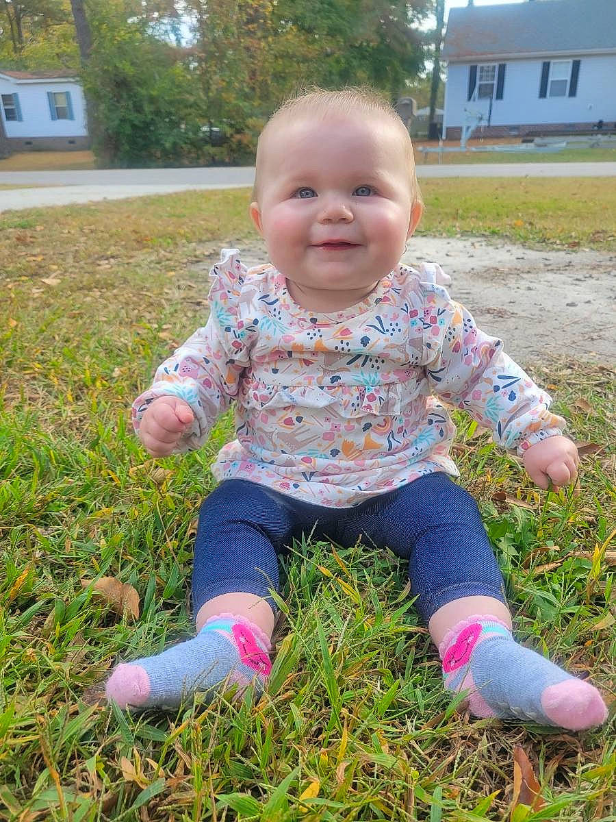Ava joined the competition — help win amazing prizes! baby, baby_toddler_clothing, child, finger, fun, grass, grassland, happy, joy, lawn, pattern, people_in_nature, person, pink, plant, sitting, smile, soil, t_shirt, toddler