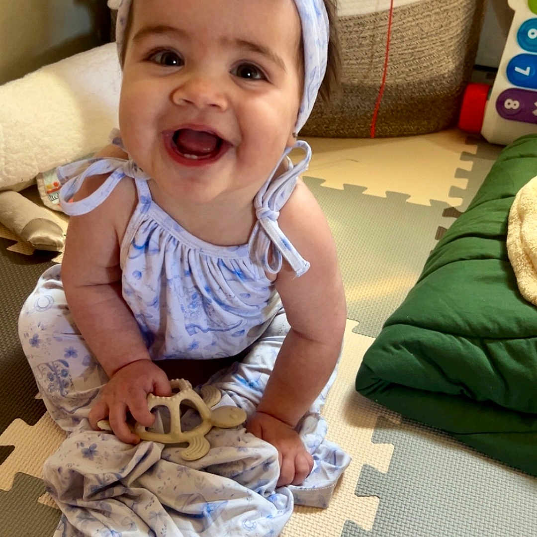 Gwen joined the competition — help win amazing prizes! baby, bow, child, clothing, colorful, cute, dress, face, floor, hand, happy, headband, home, indoor, infant, play_mat, sitting, smiling, toy, turtle