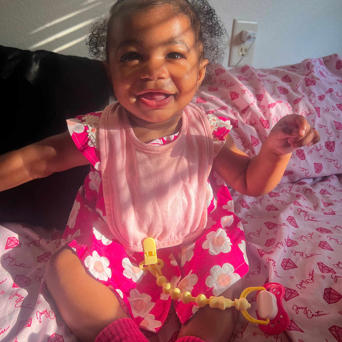 Dreamora is registered to the contest to win money with this photo: baby, child, smiling, pink_dress, socks, pacifier, blanket, patterned_blanket, sunlight, shadow, indoor, face, happy, cute, sitting, infant, curly_hair, toy, playful, portrait