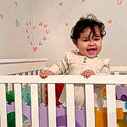 Fernanda joined the competition — help win amazing prizes! baby, crib, child, smiling, curly_hair, foam_puzzle, heart_stickers, white_crib, indoor, happy, infant, play_area, colorful, puzzle_pieces, wall_decor, hand_grip, standing, cute, room, young_child