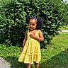 child, girl, yellow_dress, outdoor, grass, bush, smile, curly_hair, hair_clips, sunny, sandals, greenery, standing, nature, happy, portrait, person, summer, cute, fashion