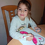 Lyana participe au concours pour gagner de l'argent avec cette photo : child, girl, drawing, heart, marker, table, chair, long_sleeve_shirt, braided_bracelet, smile, indoor, art, coloring, paper, young, person, hair, face, hand, creative