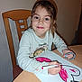 art, braided_bracelet, chair, child, coloring, creative, drawing, face, girl, hair, hand, heart, indoor, long_sleeve_shirt, marker, paper, person, smile, table, young
