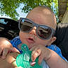 Elliot joined the competition — help win amazing prizes! baby, infant, child, sunglasses, teether, toy, blue_clothing, blanket, outdoor, portrait, sitting, car_seat, greenery, tree, leaves, sunlight, face, hands, bald, cute