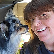 Smokey Mo Mo is registered to the contest to win money with this photo: animal, black_clothing, brown_hair, car_interior, casual, closeup, companion, dog, face, fluffy_dog, friendship, fur, happy, indoors, looking, pet, portrait, seat, smile, woman