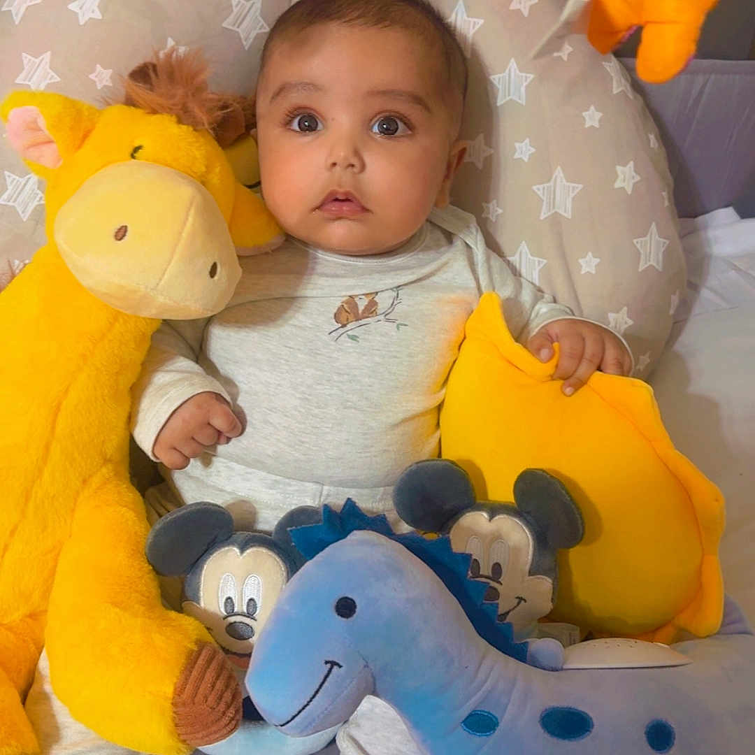 Zohan is registered to the contest to win money with this photo: baby, bed, blue, child, cushion, cute, dinosaur, face, feet, giraffe, indoor, infant, orange, pajamas, person, plush_toy, soft_toy, star_pattern, stuffed_animal, yellow