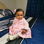 Ariyah is registered to the contest to win money with this photo: toddler, child, girl, pink_dress, flower_hair_accessory, smiling, sitting, bed, bedroom, blue_bedding, white_shoes, happy, cute, portrait, indoor, person, young_child, fashion, home, decor