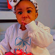 Treasure is registered to the contest to win money with this photo: baby, child, infant, sweater, headband, leopard_print, cherry_print, thumb_sucking, indoors, sitting, cute, adorable, portrait, person, clothing, red_pants, wall_art, heart_emojis, cozy, young_child